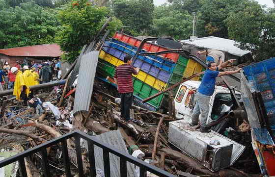 Люди ходят среди того, что осталось от грузовиков на улице, разрушенной в результате проливных дождей в Верапасе